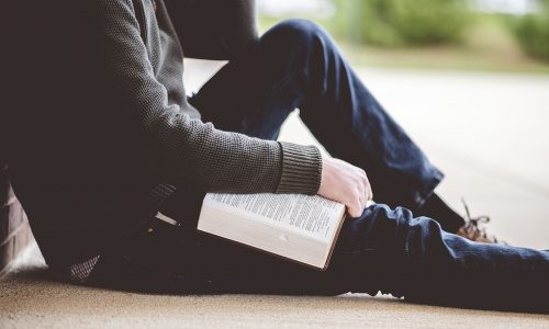 A young male sitting on the ground and holding the bible in his hands